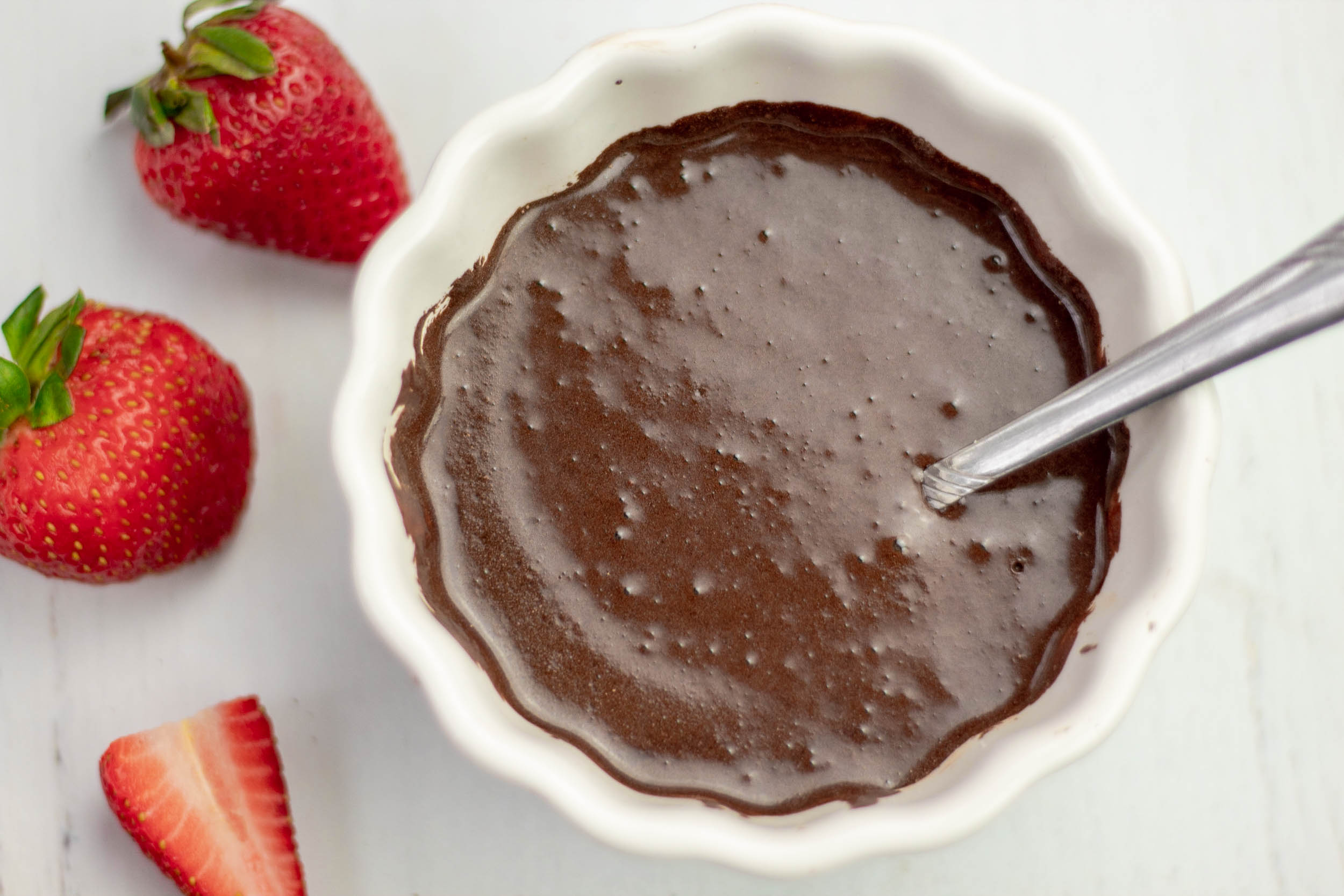 chocolate ganache in a bowl with strawberries around it