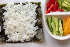 Nori sheet with rice spread on it sitting next to a platter with cut vegetables