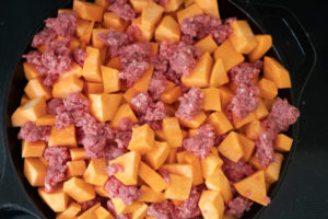 Raw sweet potatoes and ground beef in a skillet before cooking