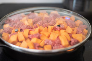 Raw sweet potatoes and ground beef in a skillet covered with a lid