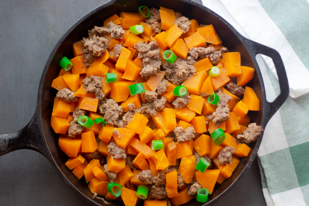 Cooked sweet potatoes and ground beef in an iron skillet