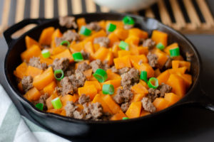 Cooked sweet potatoes and ground beef in an iron skillet