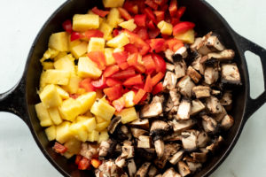 An iron skillet with peppers, mushrooms, and pineapples
