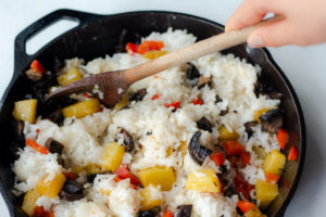 Someone stirring rice with cooked vegetables in an iron skillet