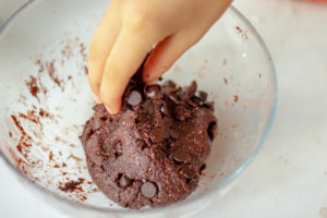 Someone getting a piece of chocolate cookie dough from the bowl