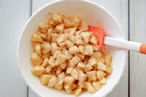 A white bowl with apples covered with sugar and oat flour, and sugar mixed in