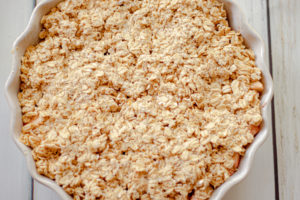 A pie pan with apple crisp filling and topping on ready to be baked