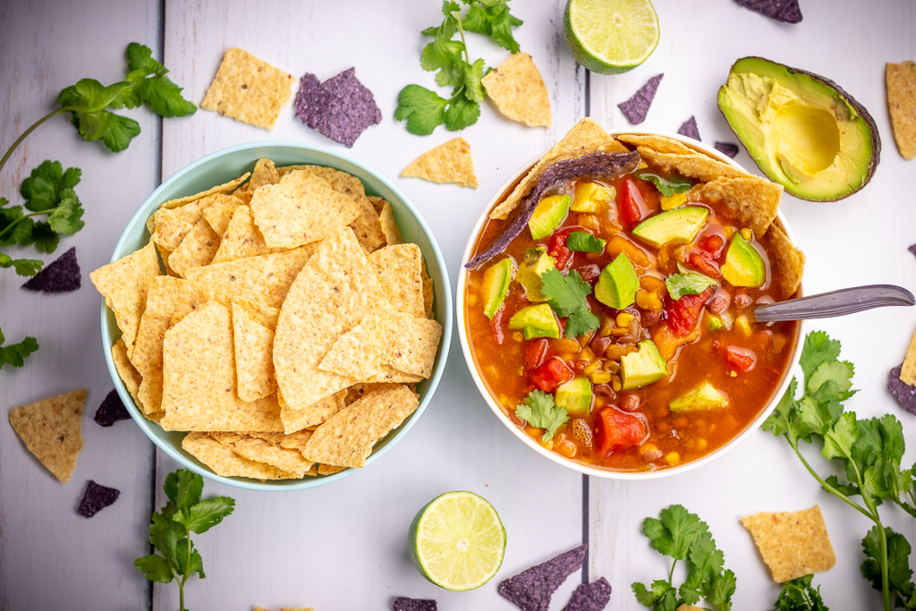 Vegan chili in a bowl next to a bowl of tortilla chips with cilantro and avocado around the bowls