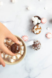 Someone holding a vegan hot chocolate bomb over a cup of hot chocolate