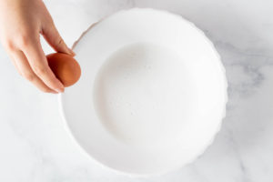 Cracking an egg over a bowl with milk in it